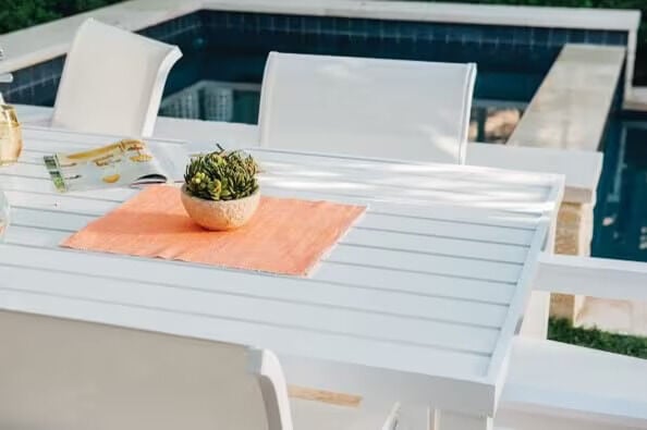 white table by the pool with a peach colored placemat and a plant