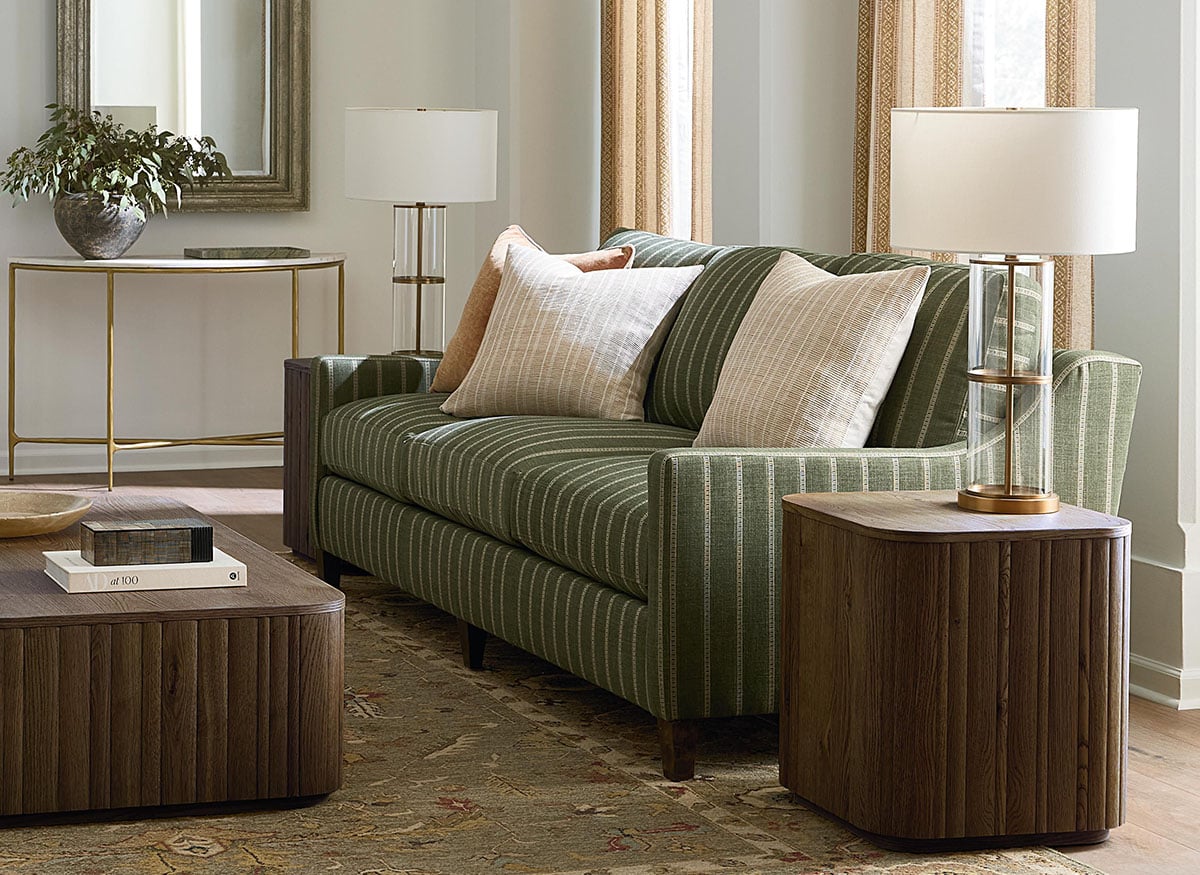 Green striped sofa with neutral throw pillows, wood accent tables, and lamps in a bright living room.